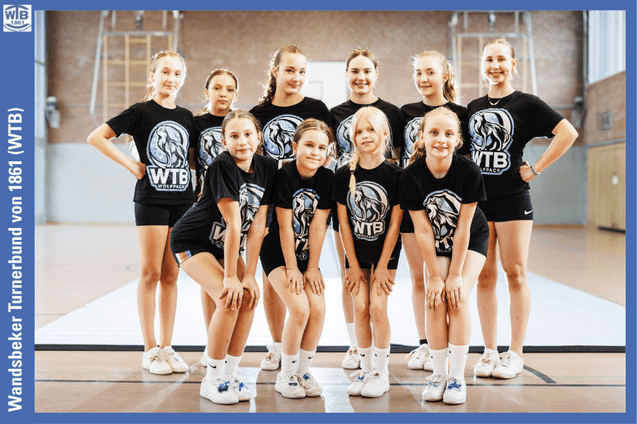 Gruppe von zehn M&auml;dchen in T-Shirts mit WTB-Logo, l&auml;chelnd in einer Turnhalle auf einem Sportboden posierend.