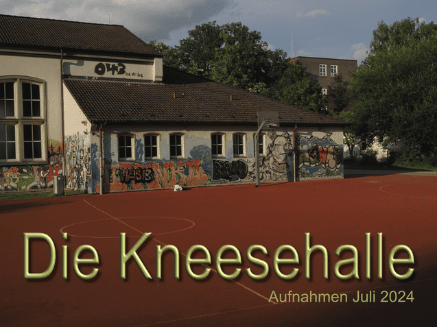 Au&szlig;enansicht der Kneesehalle mit graffiti-bemalter Wand und orangefarbenem Sportplatz im Vordergrund.