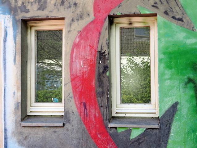 Zwei Fenster mit reflektierenden Scheiben, umgeben von bunten Graffiti auf einer Wand.