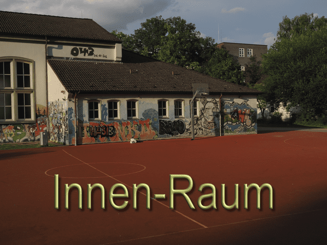Graffiti-bedeckte Wand eines Schulgeb&auml;udes neben einem Basketballfeld auf einem roten Sportplatz im Freien.