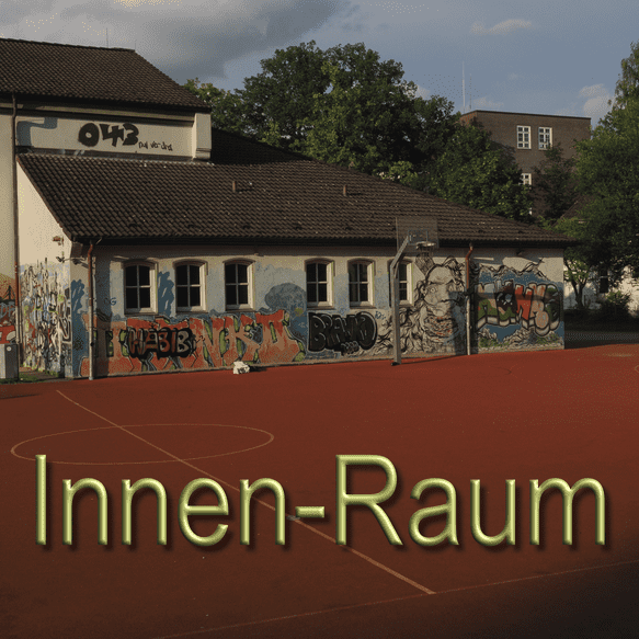 Graffiti-bedeckte Wand eines Schulgeb&auml;udes neben einem Basketballfeld auf einem roten Sportplatz im Freien.