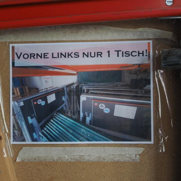 Hinweis auf einem Blatt: &bdquo;Vorne links nur 1 Tisch!&ldquo; neben mehreren Tischtennisplatten in einem Raum.