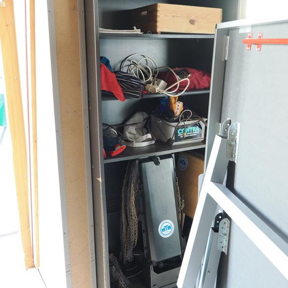 Aufbewahrungsschrank mit verschiedenen Gegenst&auml;nden, darunter Kleidung, Kabel und eine schwarze Box, sichtbar.