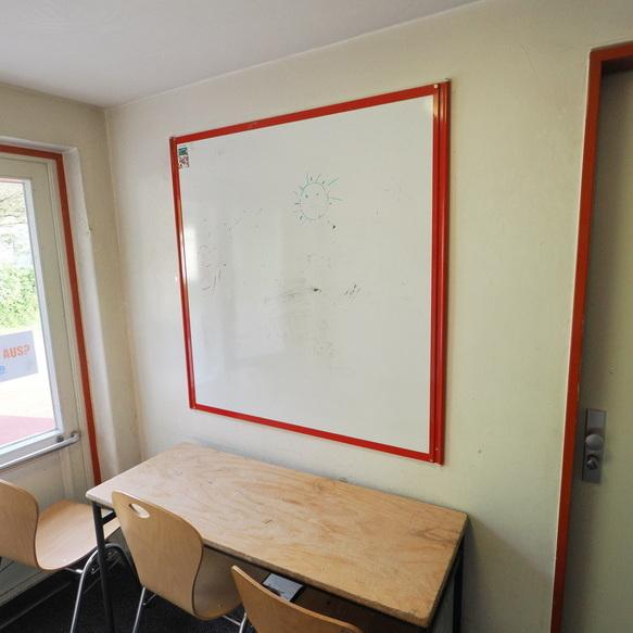 Leere Klasse mit einem Tisch, zwei St&uuml;hlen, einem wei&szlig;en Brett an der Wand und einer T&uuml;r mit der Aufschrift "LEHRER".