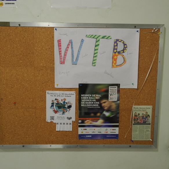 Korkwand mit Aush&auml;ngen, darunter ein buntes &bdquo;WTB&ldquo;-Plakat und ein Tischtennis-Eventteilnehmer-Infoflyer.