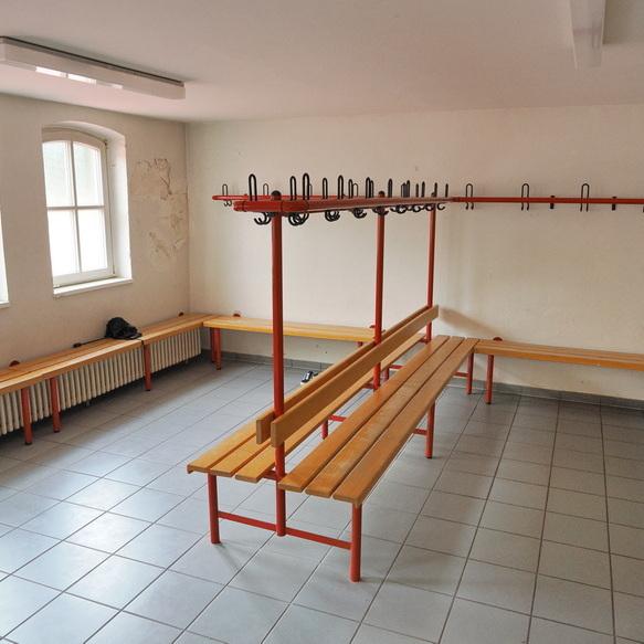 Leere Umkleidekabine mit Holzb&auml;nken, Kleiderhaken und Fliesenboden. Helle Fenster sorgen f&uuml;r Licht.