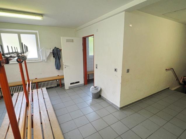 Innenansicht eines Umkleidebereichs mit Sitzelementen, Abstellhaken und Zugang zu einem Badezimmer.