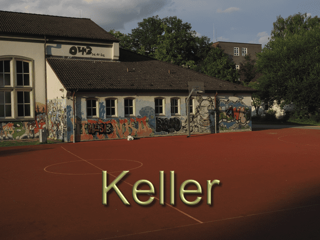Schulgeb&auml;ude mit bunten Graffiti an der Wand, davor ein orangefarbener Sportplatz mit Basketballkorb.
