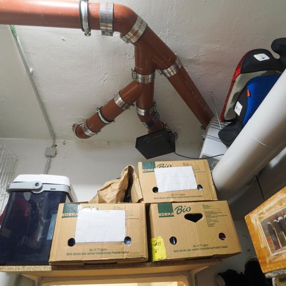 Rohrleitungen verlaufen unter der Decke in einem Lagerraum mit zwei stapelbaren Kartons und verschiedenen Beh&auml;ltern.