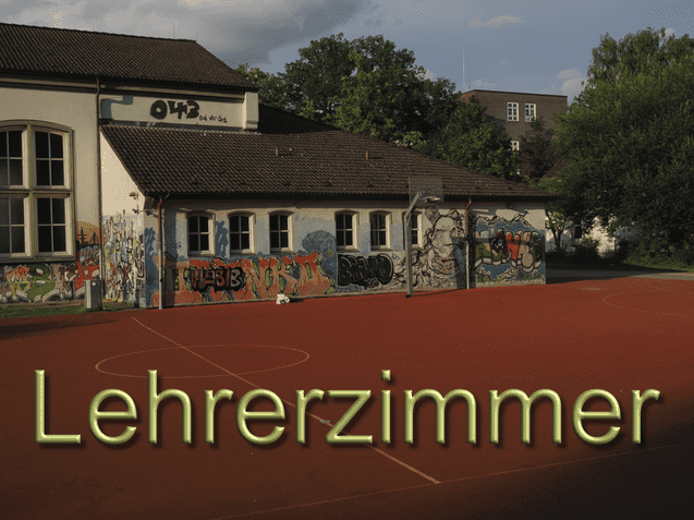 Graffiti-bedeckte Wand eines Lehrerzimmers an einem roten Sportplatz unter einem bew&ouml;lkten Himmel.