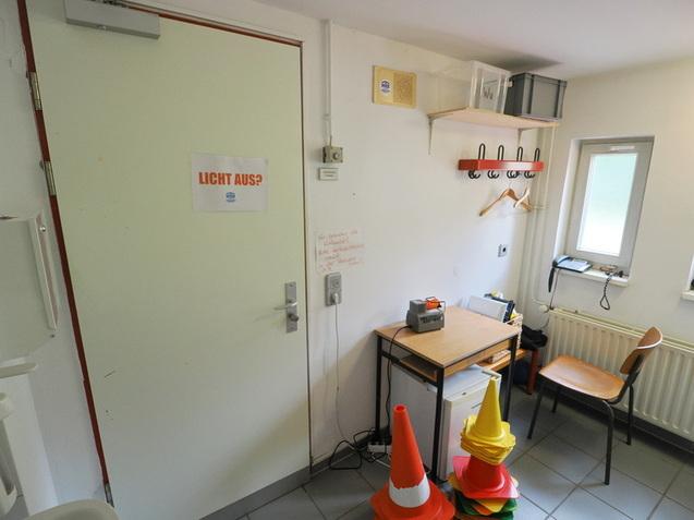 Raum mit einer T&uuml;r, einem Tisch, einem Stuhl, einem Regal und bunten Pylonen, daneben ein Lichtschalter und ein Fenster.