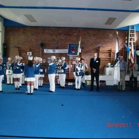Gruppe von Personen in Uniformen steht in einer Turnhalle bei einer offiziellen Zeremonie mit Flaggen und Dekorationen.