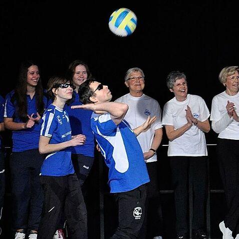 Gruppe von Menschen applaudiert, während ein Spieler mit Bandagen einen Volleyball anhebt.