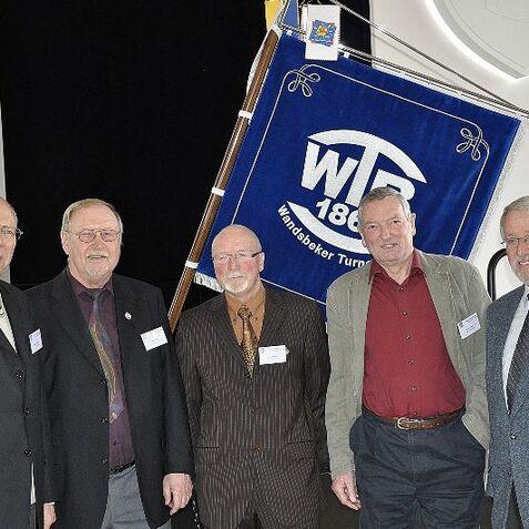 Fünf Männer stehen lächelnd vor einer blauen Fahne des Wandsbecker Turnerbundes.