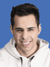 Porträt eines lächelnden jungen Mannes mit kurzem, dunklem Haar vor einem einfarbigen blauen Hintergrund.