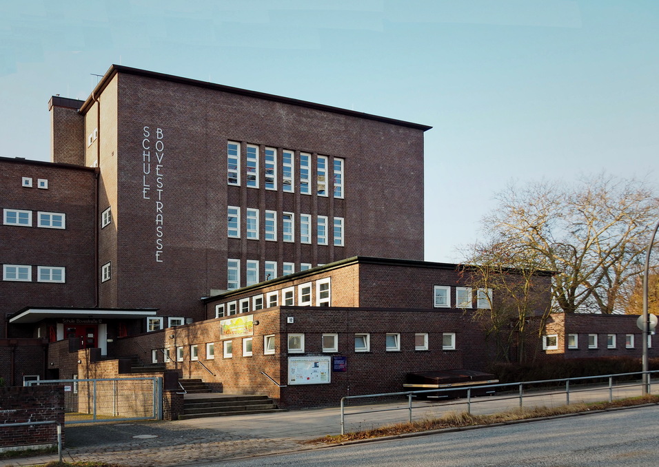 Fassade eines rechteckigen Schulgeb&auml;udes mit Fenstern und dem Schriftzug &bdquo;Schule Bovetstra&szlig;e&ldquo;.