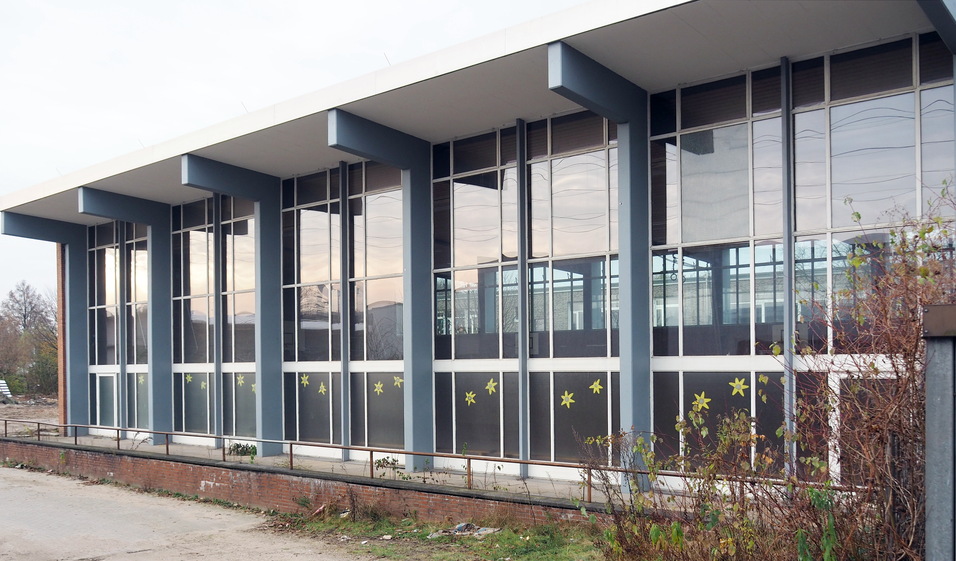 Moderne Geb&auml;udeansicht mit gro&szlig;en Fenstern und grafischen Dekorationen an der Fassade, umgeben von Gr&uuml;n.