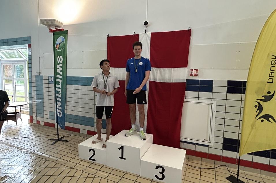 Zwei Schwimmer stehen auf dem Siegertreppchen, der erste in blauer Schwimmbekleidung, hinter ihnen eine d&auml;nische Flagge.