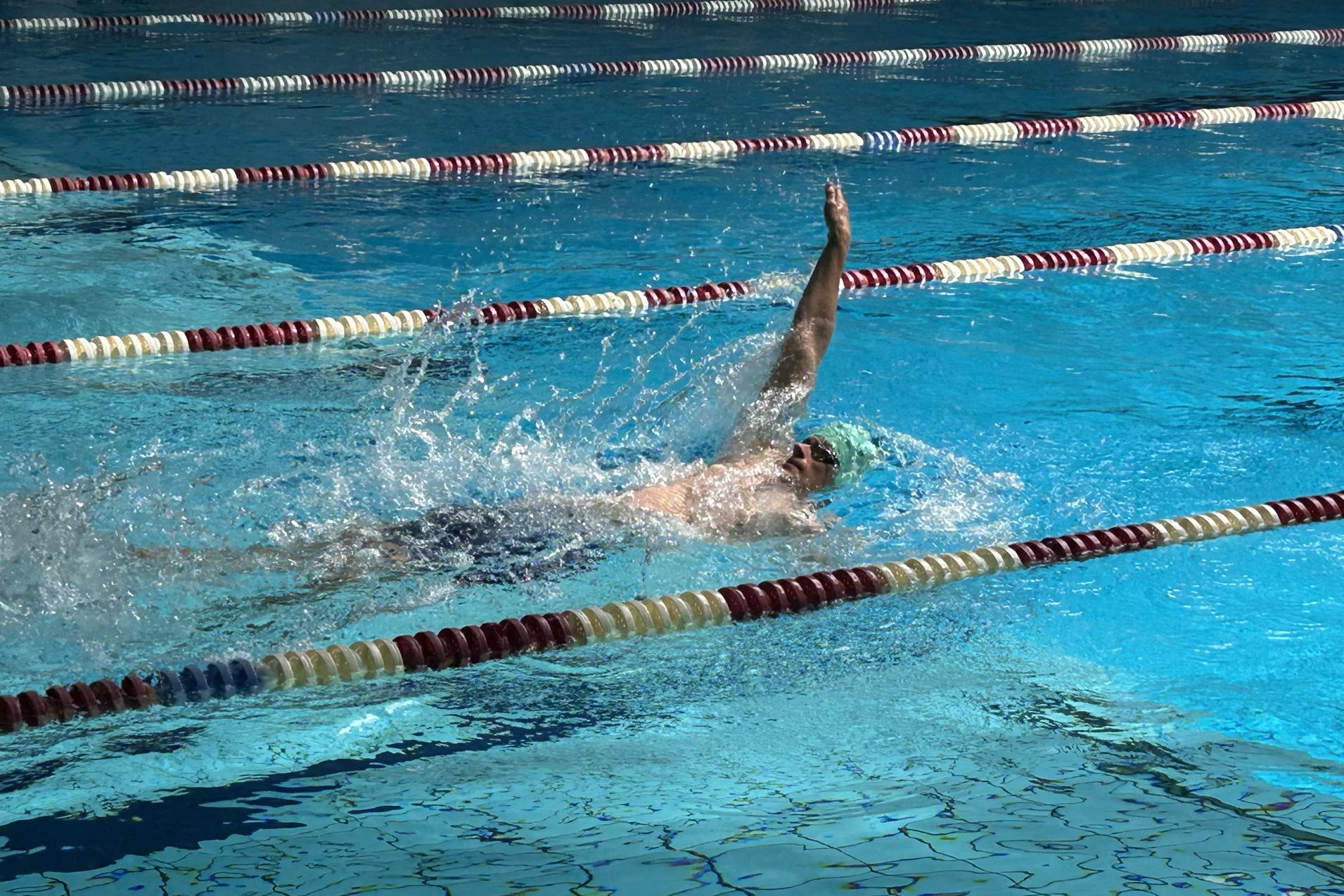 Schwimmer im Wasser beim Rückenschwimmen, spritzend, mit einer Schwimmkappe in einem blauen Schwimmbecken.