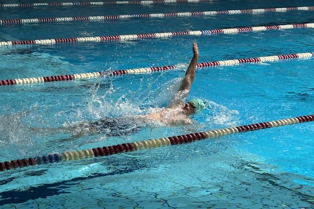 Schwimmer im Wasser beim R&uuml;ckenschwimmen, spritzend, mit einer Schwimmkappe in einem blauen Schwimmbecken.