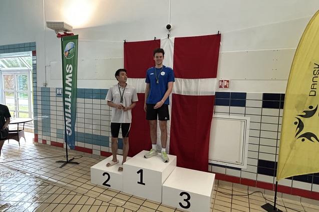Zwei Schwimmer stehen auf dem Siegertreppchen, der erste in blauer Schwimmbekleidung, hinter ihnen eine d&auml;nische Flagge.