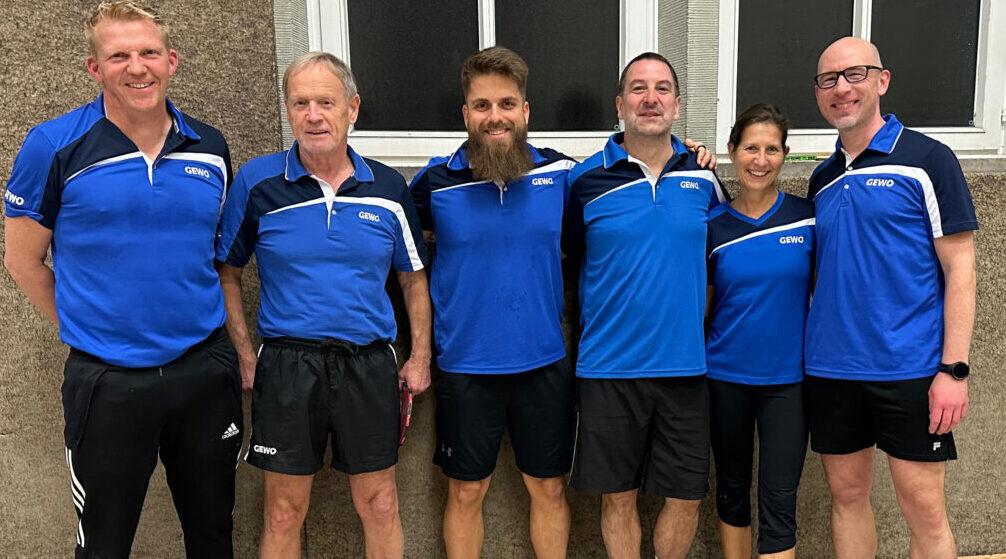 Gruppe von sechs Tischtennisspielern in blauen Trikots, posierend in einer Sporthalle.