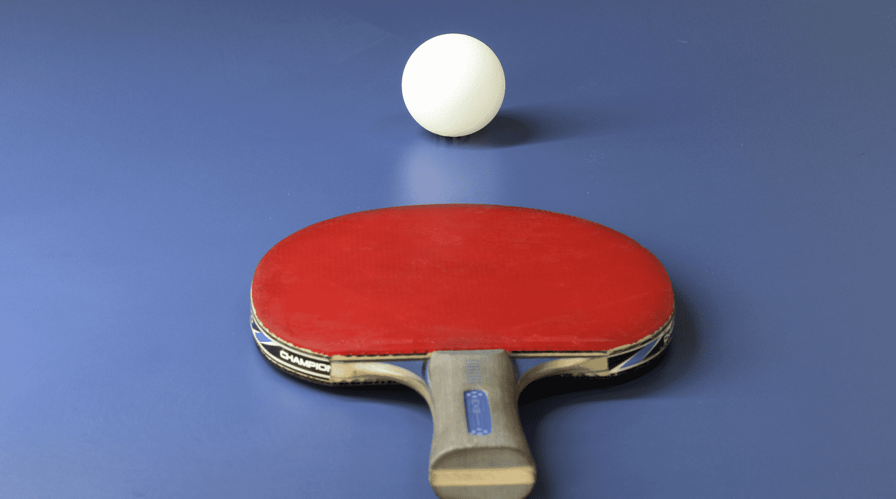 Tischtennisschläger mit roter Schlagfläche und weißer Tafel auf einem blauen Tischtennistisch.