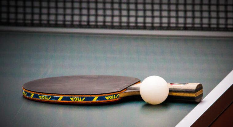 Nahaufnahme eines Tischtennisschlägers mit einem weißen Ball auf einer grünen Tischtennisplatte.