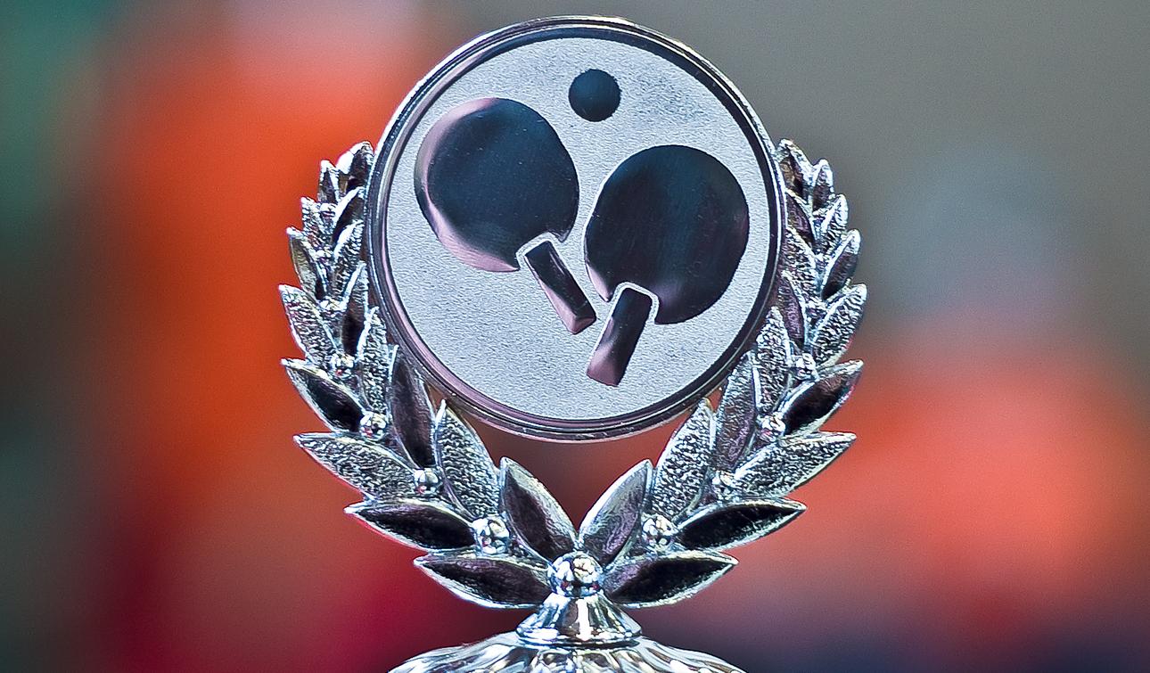 Silberne Tischtennis-Trophäe mit eingraviertem Tischtennis-Symbol, umgeben von einem Lorbeerkranz.