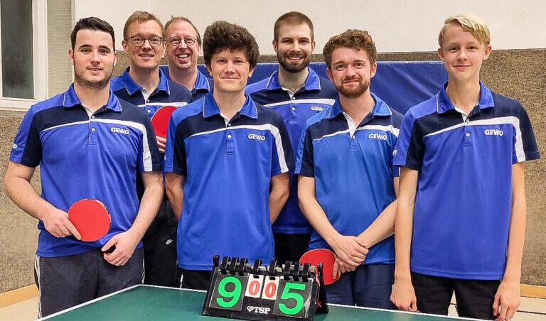 Sechs Tischtennisspieler in blauen Trikots stehen lächelnd neben einem Tischtennistisch mit Punktestand 9:5.