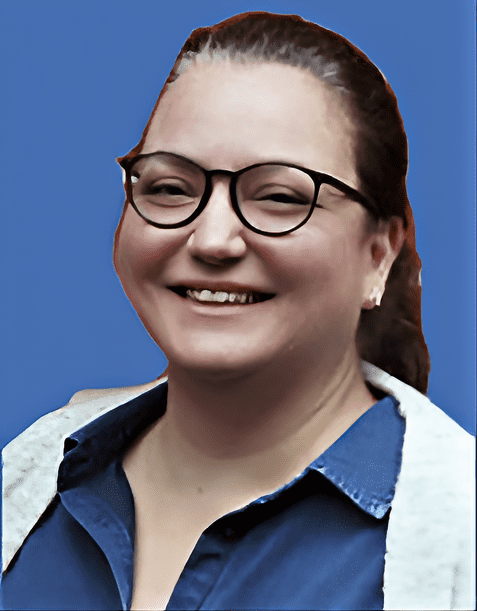 Lächelnde Frau mit Brille und hochgestecktem Haar vor einem blauen Hintergrund, trägt ein Hemd mit Kapuze.