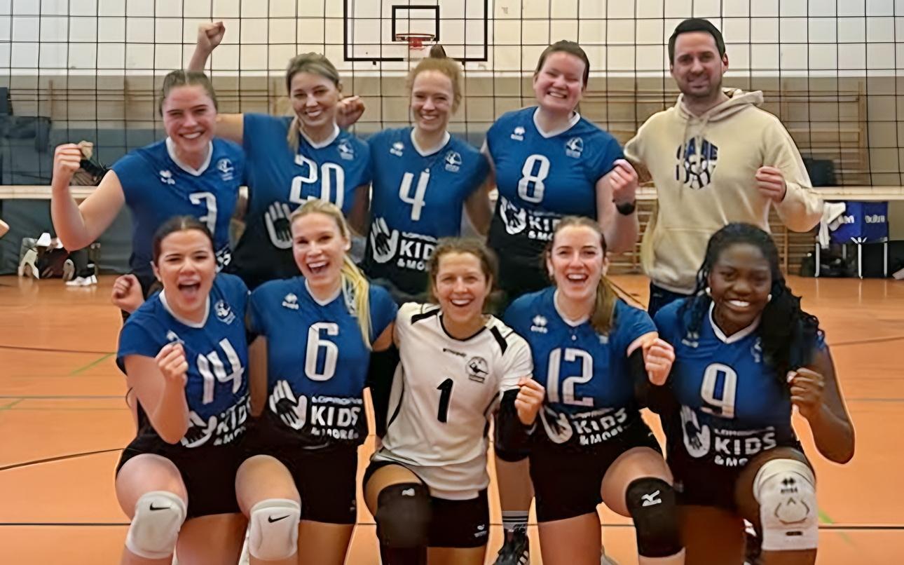Gruppennfoto eines Volleyballteams mit 10 Spielerinnen in blauen Trikots, die fröhlich posieren, begleitet von einer männlichen Trainer.