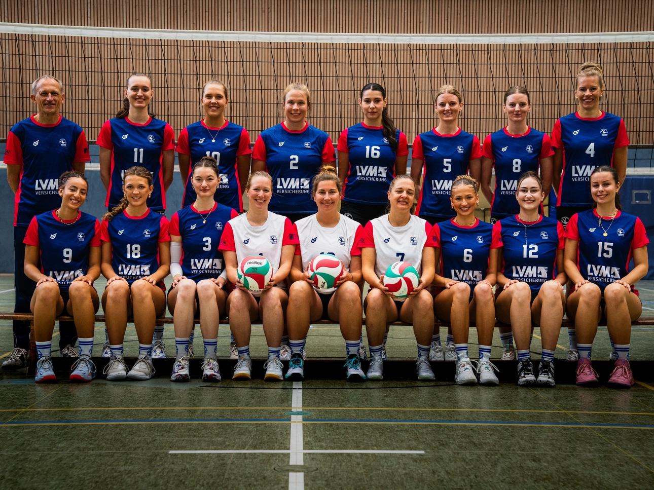 Mannschaftsbild von 15 Volleyballspielern in roten und blauen Trikots, zwei Bällen in der Vordergrund.