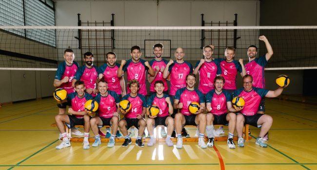 Gruppenfoto von 16 Volleyballspielern in pinken Trikots, die mit Volleyballbällen auf einem Sportfeld posieren.