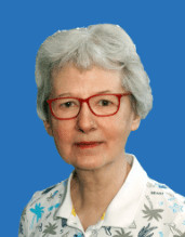 Porträt einer Frau mit grauen Haaren und roten Brillen, vor blauem Hintergrund, trägt ein gemustertes Hemd.