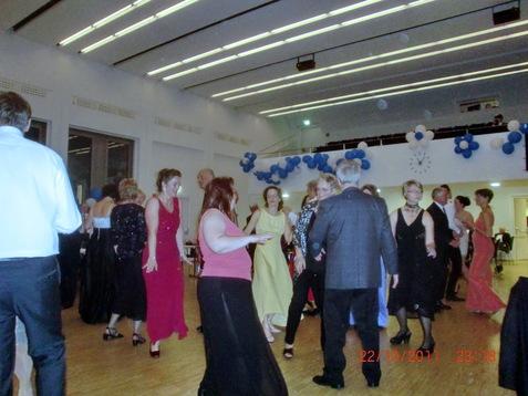 Tanzende Menschen in eleganter Abendkleidung während einer Feier, dekoriert mit blauen und weißen Ballons.