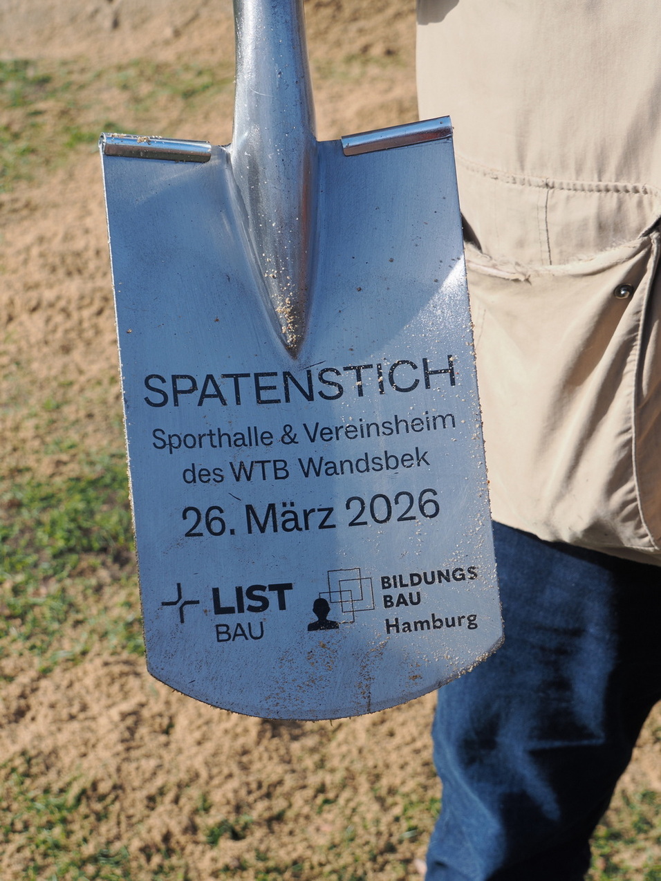 Schaufel mit Gravur f&uuml;r den Spatenstich des WTB Wandsbek am 26. M&auml;rz 2026, gehalten von einer Person.