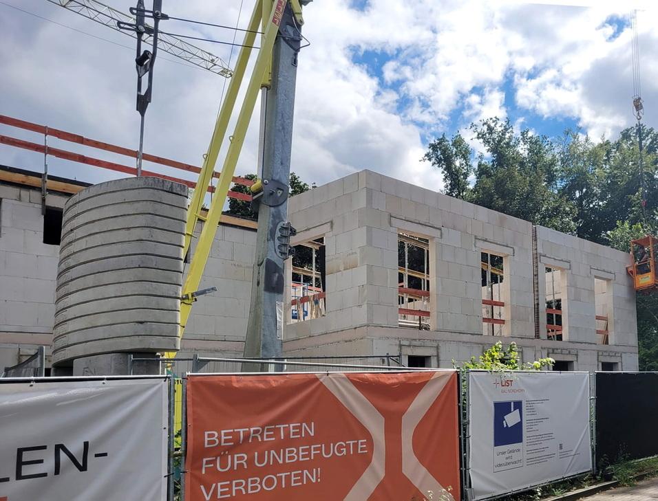Baustelle mit Rohbau aus Betonsteinen, Fenstern und Baustellenschild mit Warnhinweis auf unverantwortliches Betreten.