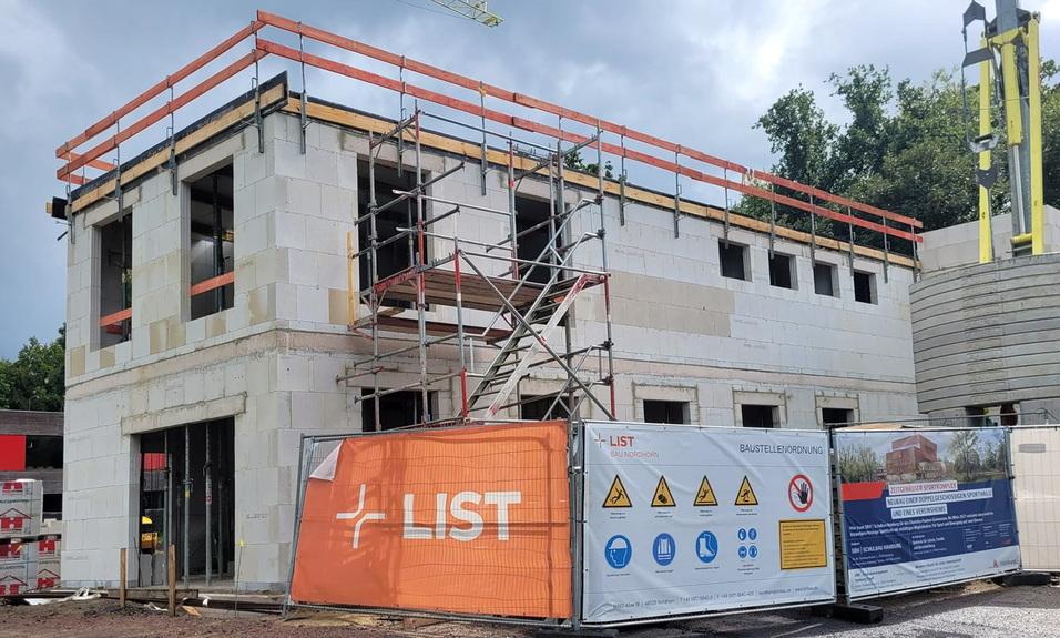 Bau eines zweistöckigen Hauses mit Arbeitsgerüst und Sicherheitszäunen auf einer Baustelle unter bewölkten Himmel.