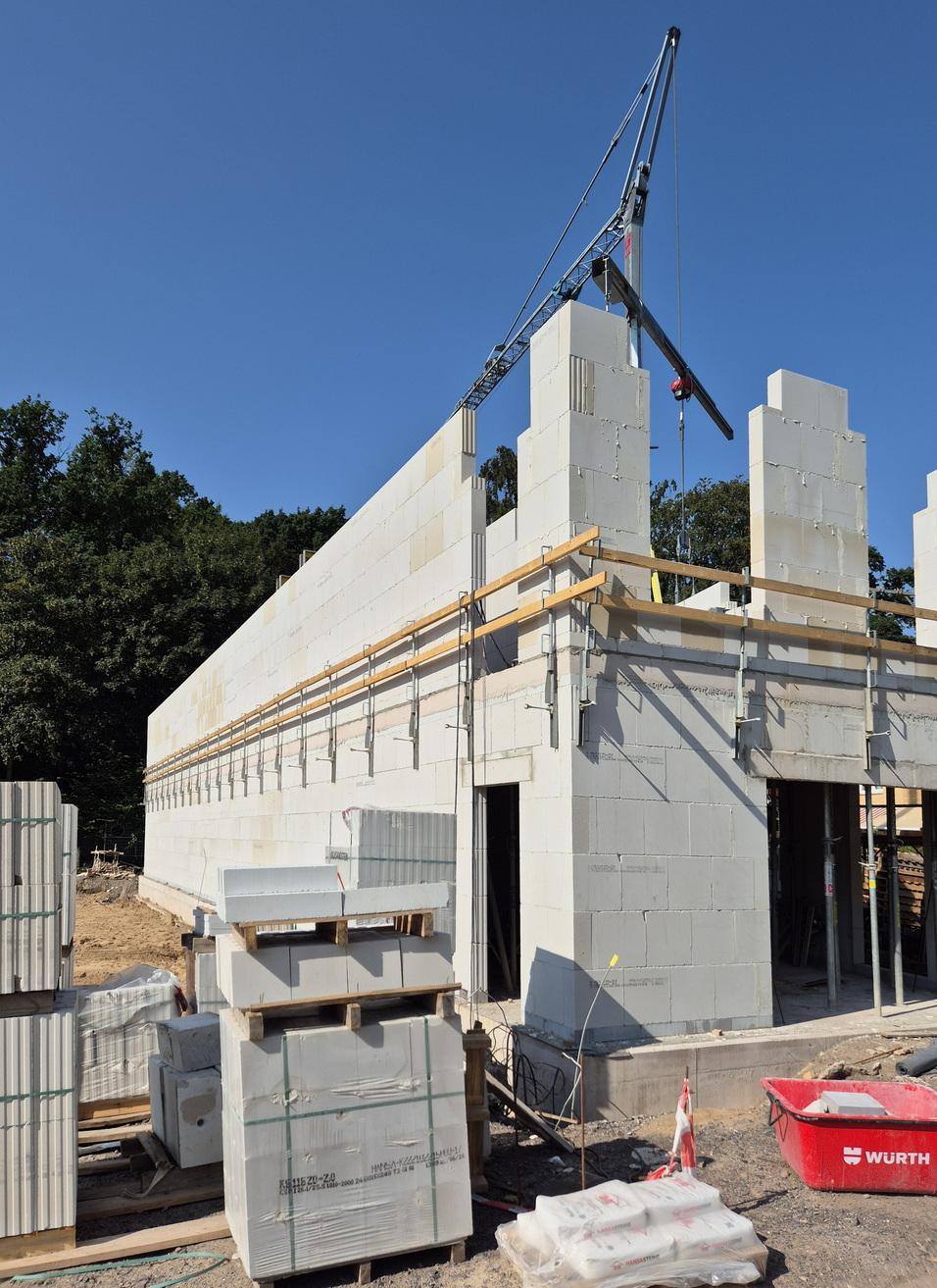 Blick auf eine Baustelle mit einem Rohbau aus weißen Blöcken und einem Kran, um Materialien zu heben.