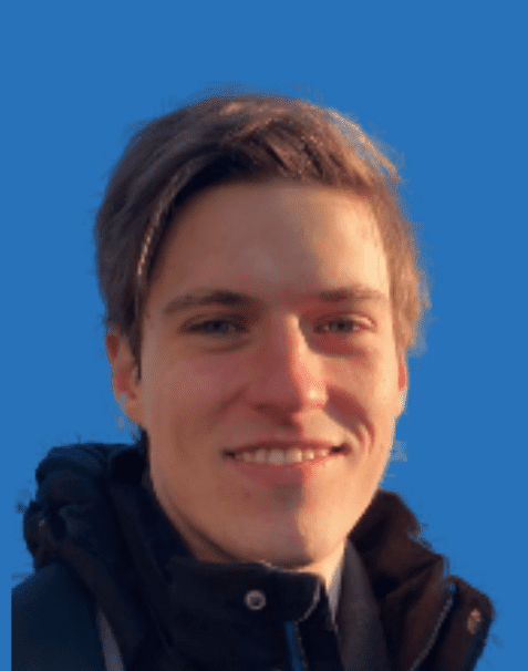 Portrait eines lächelnden jungen Mannes mit blonden Haaren, vor einem einfarbigen blauen Hintergrund.