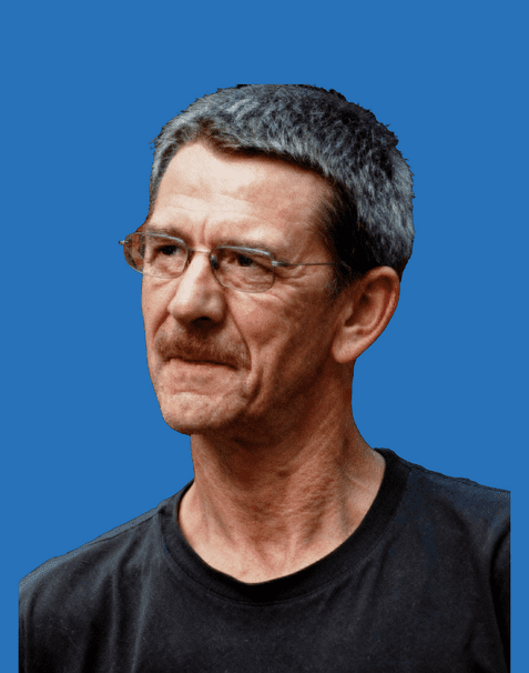 Portrait eines Mannes mit grauem Haar und Brille, der ernst in die Kamera schaut, vor einem blauen Hintergrund.