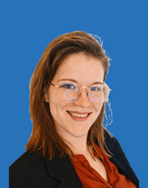 Portrait einer lächelnden Frau mit Brille, braunen Haaren und Anzugjacke vor einem blauen Hintergrund.