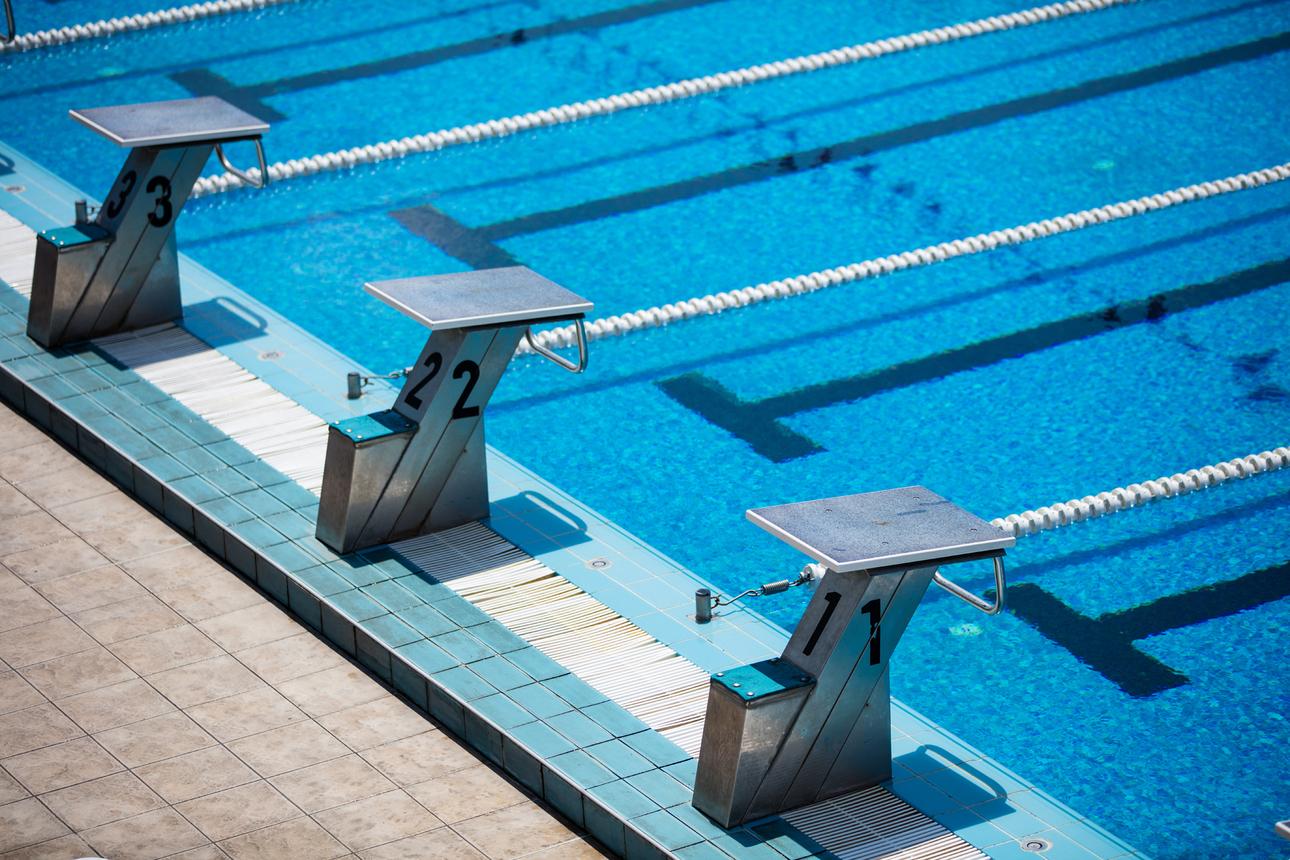 Drei Startblöcke mit den Nummern 11, 22 und 33 stehen am Beckenrand eines blauen Schwimmbeckens.